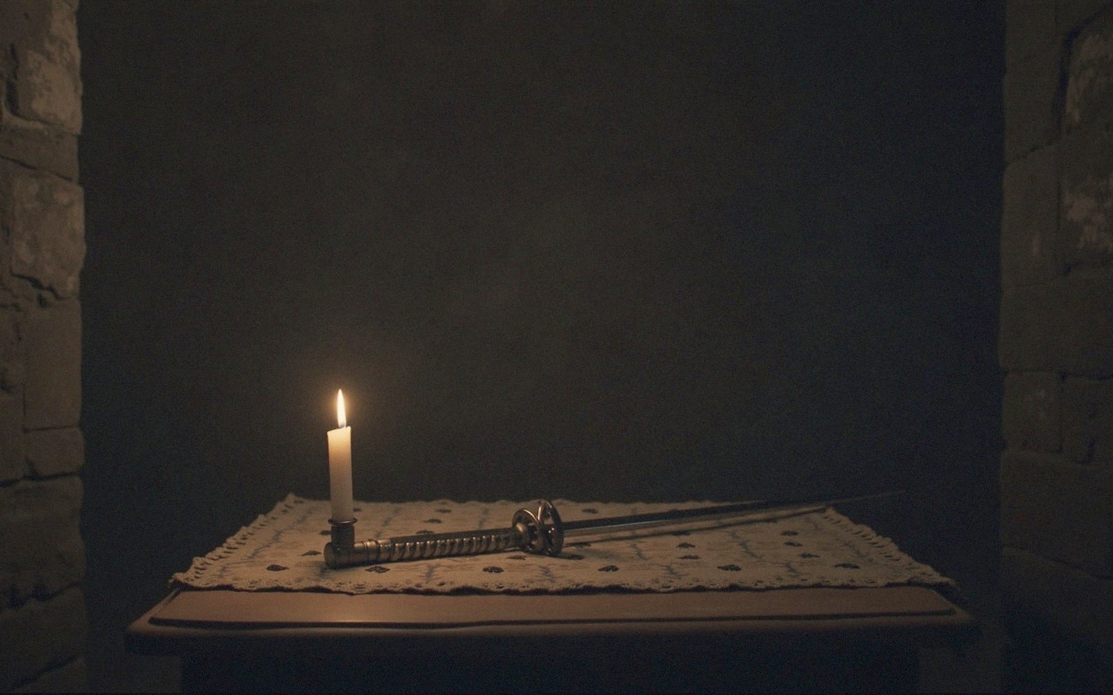 A candlelit stone interior with a rapier resting on a table